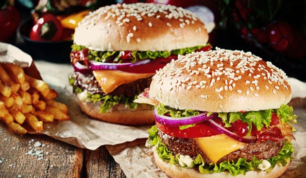 Two burgers with lettuce, cheese, and onions beside a pile of fries.