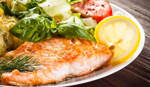 close up of cooked fish entree with lemon slice and herbs