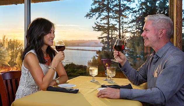 Couple smiling, holding wine glasses, overlooking a lake.