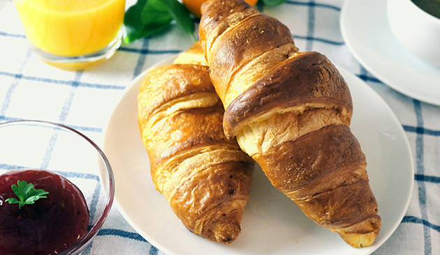 two plain croissants on white plate on blue check tablecloth