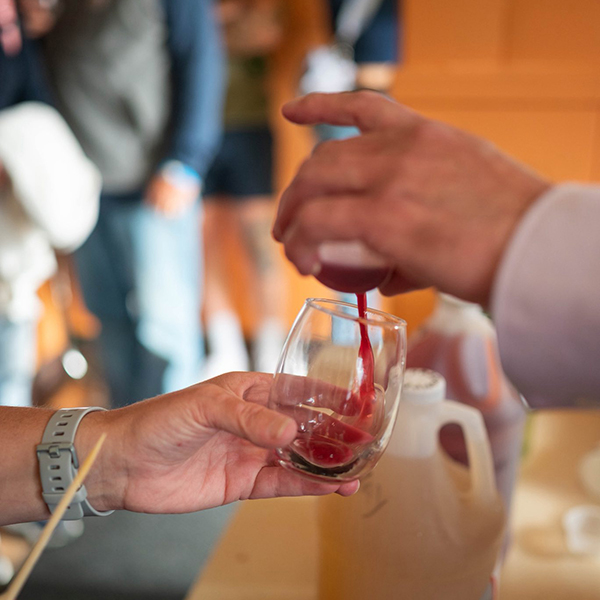 Hand holding wine glass while another hand pours wine.