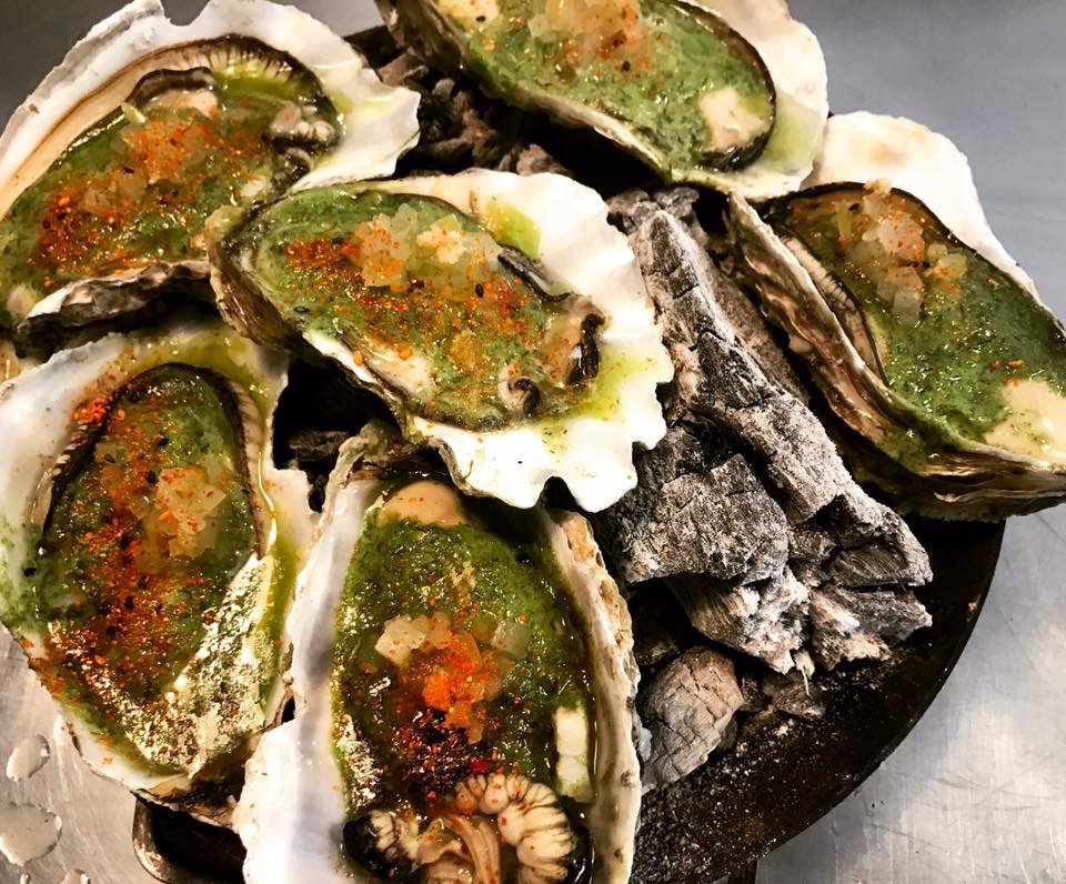 Clausen's Oyster Deli oysters on the half shell are served over charcoal, topped with green herb sauce, diced garnish and seasoning for a freshly prepared seafood dish.