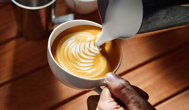 Hand holding a cup with creamy coffee art on wooden table.