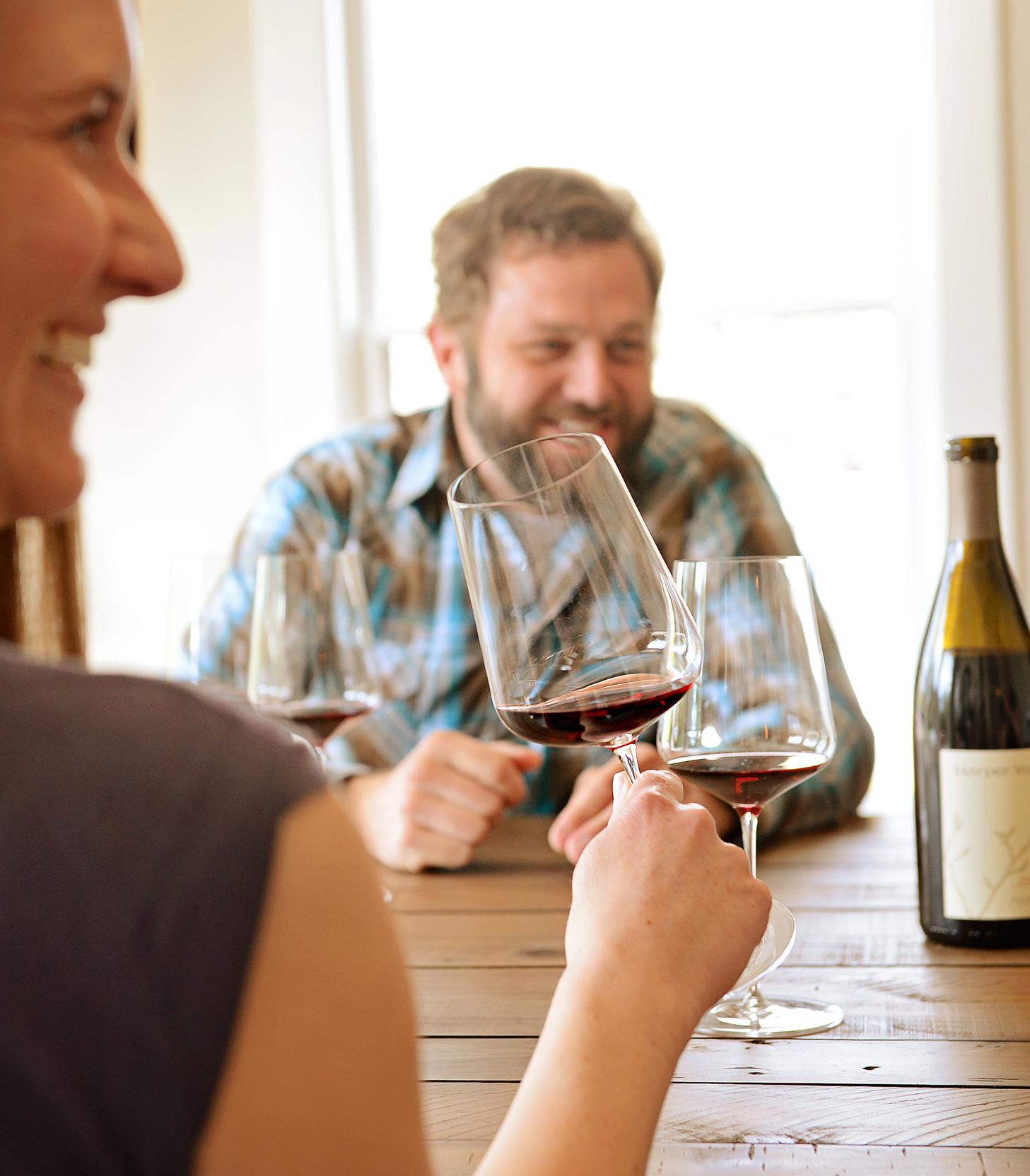 two people seated a table smiling. one holds a glass of wine