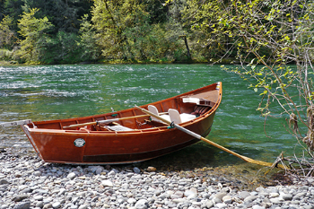 Brown canoe on rocky shore by a river.
