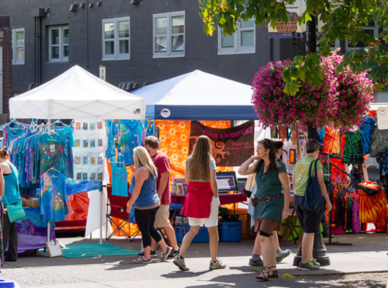 outdoor market with vendors under pop up tents and people walking by