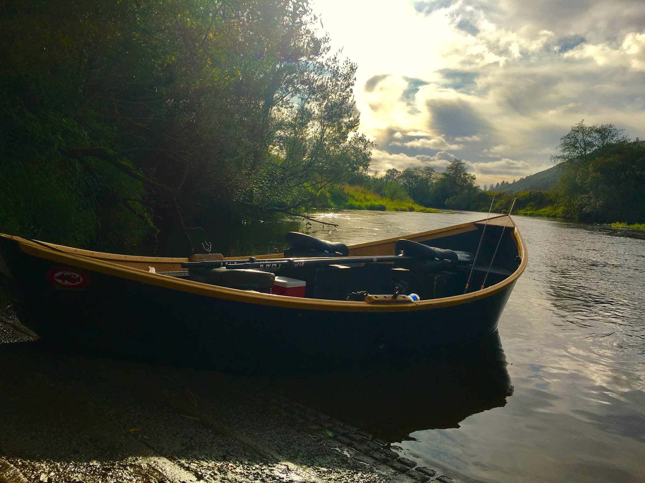 dory boat half on shore with scenic water and forest in background