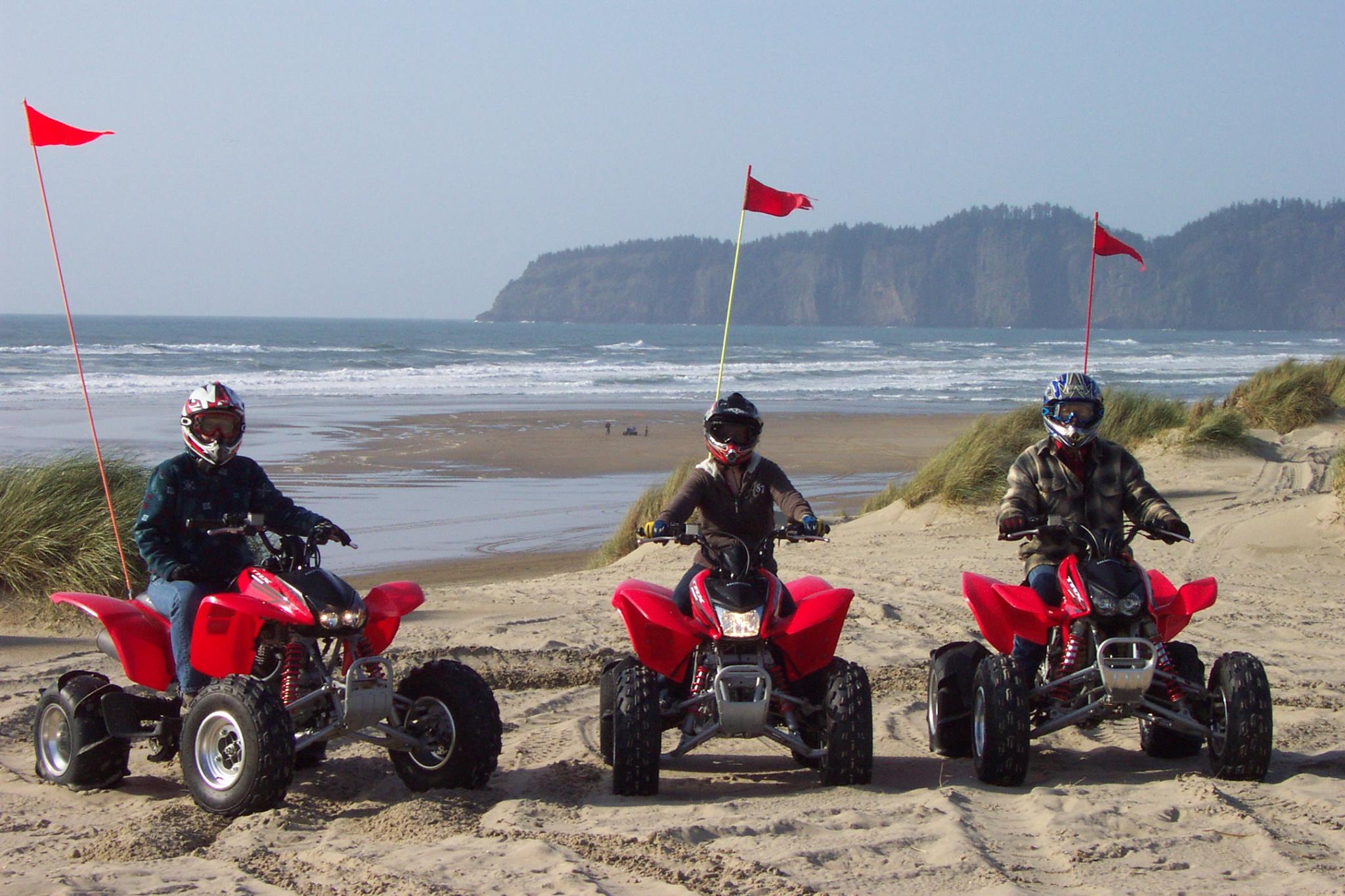 three riders on ATVs look at camera with ocean in background