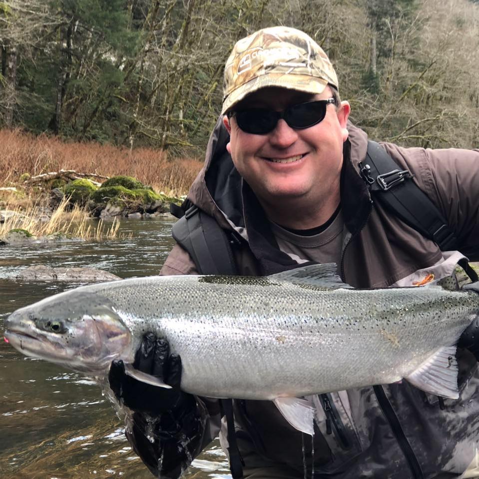 person wearing hat, sunglasses and gloves smiles while holding up fish they caught