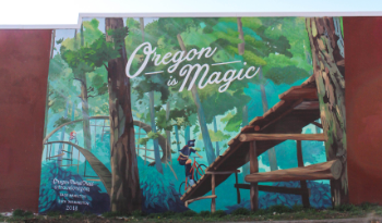 Mural with "Oregon is Magic" text and person biking on wooden path.