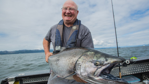 person standing on boat smiling and holding salmon they just caught