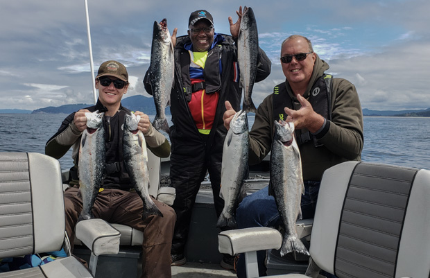 three people on a boat holding up the the fish they caught (2 each) while smiling at the camera