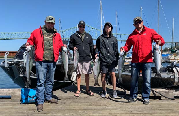 four people stand on a dock holding two fish each