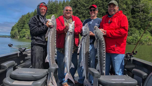 four people stand on motor boat holding a sturgeon each and smiling at camera