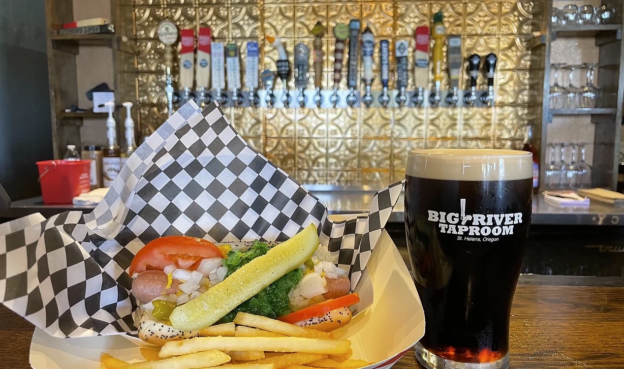 basket with hot dog and French fries atop bar next to pint of dark beer
