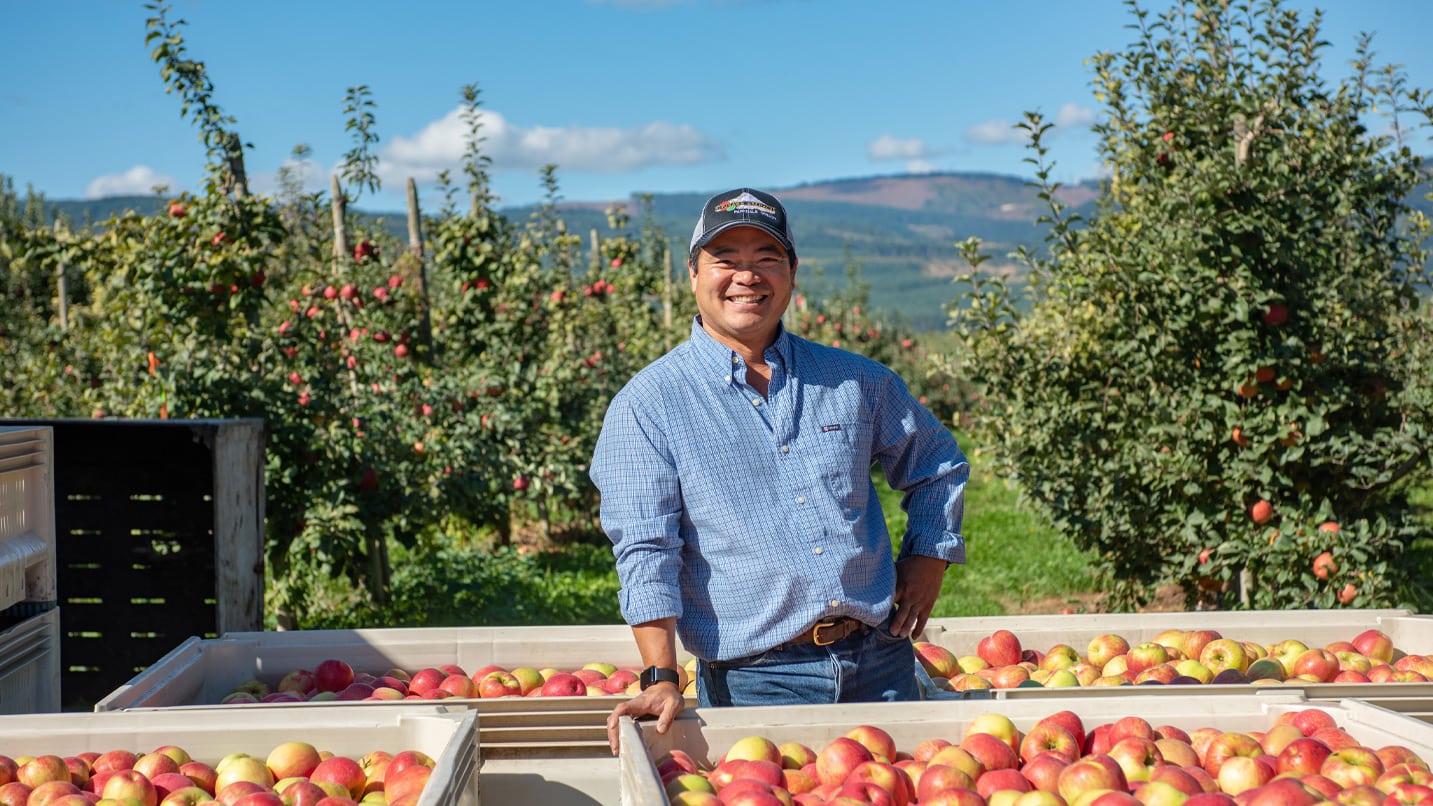 Farmer Randy Kiyokawa smiling in front of a bunch of apples