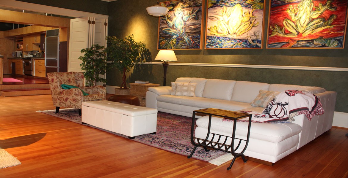 Living room with white couch, floral chair, and three large paintings.