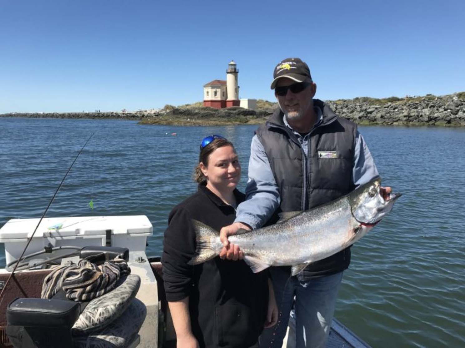 A couple holding up their catch in front of the Coquille River Lighthouse with Fish Oregon Guide Service in Bandon, Oregon