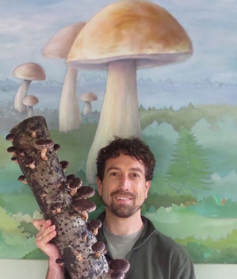 A man holding a log covered in mushrooms at the Wild Rivers Mushroom Festival in Brookings, Oregon