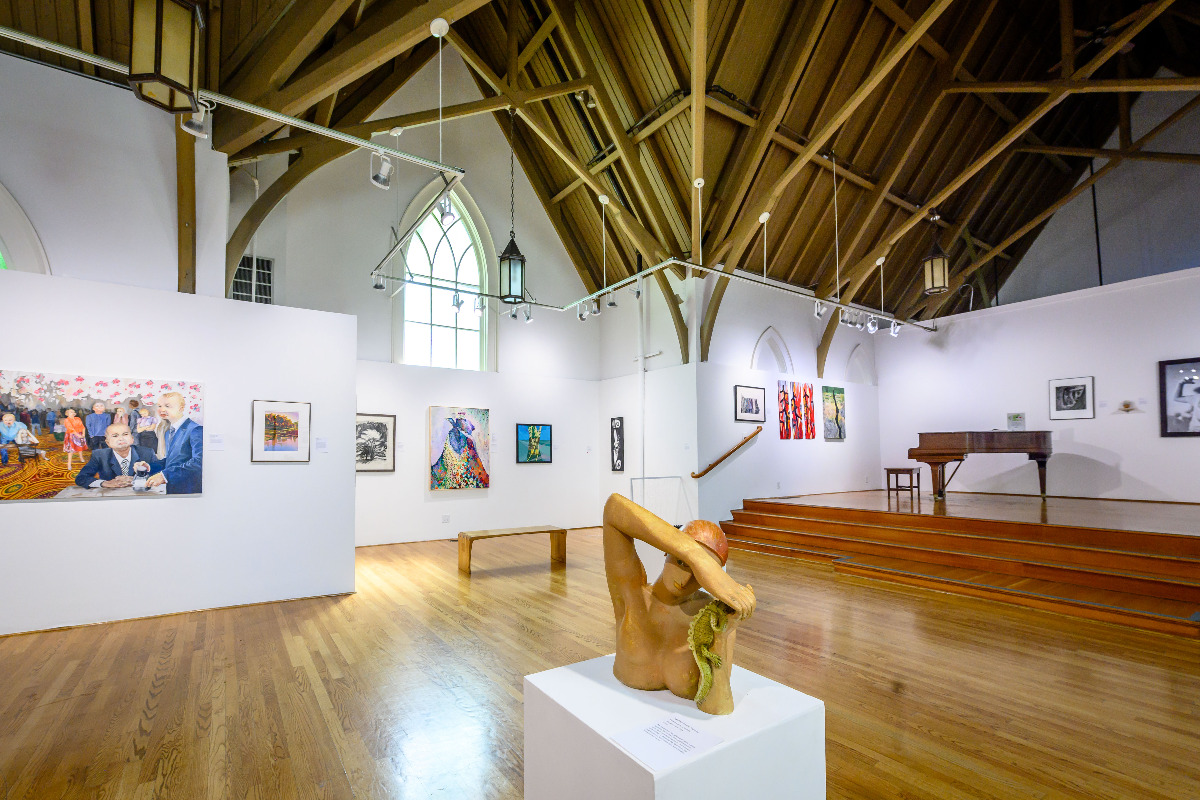 art gallery with vaulted ceilings, wooden floors and white walls and art hung on walls and sculpture on pedestal