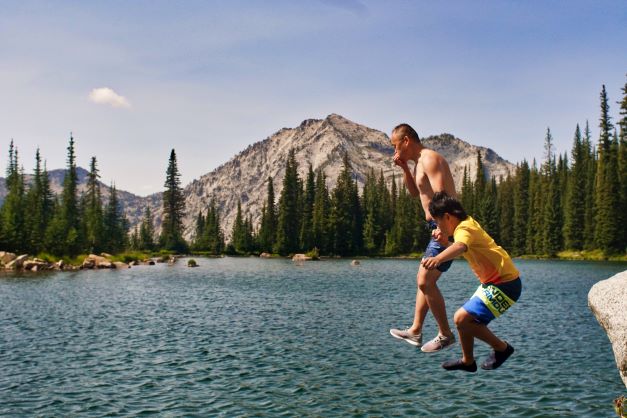 father and son jumping off of a rock into a high mountain lake