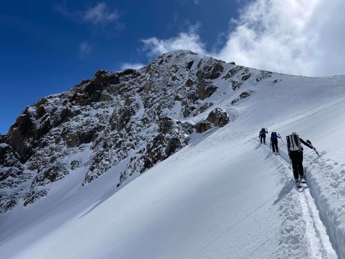 three skiers climbing up a snowy mountainside to Pete's Point