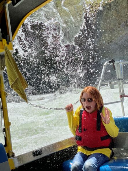 female in a yellow shirt and red life jacket getting soaked on the jet boat