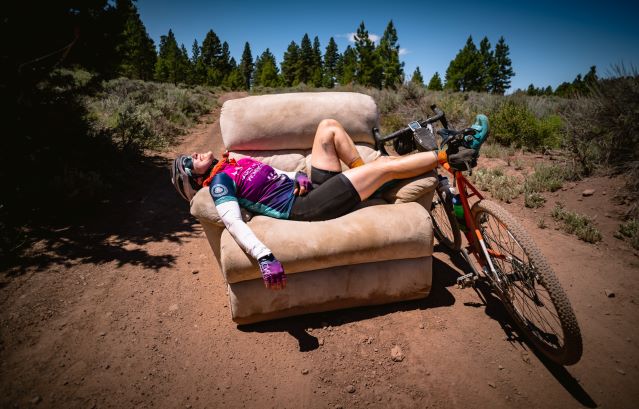cyclist laying in an oversized chair with their feet propped up on their bike