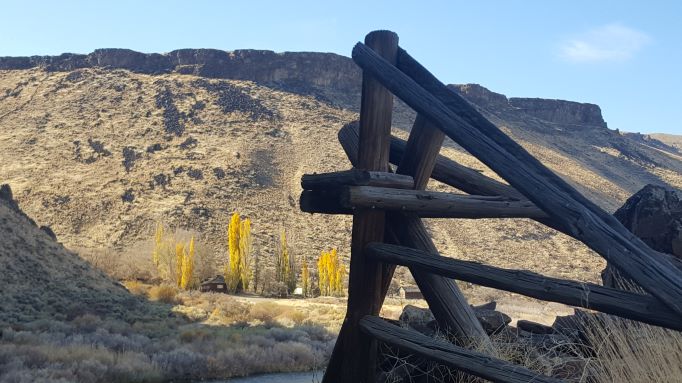 fence post in the forefront with sage brush and butte in the background
