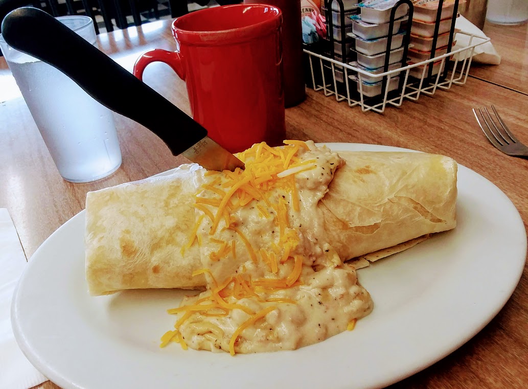Breakfast burrito topped with country gravy and cheddar cheese