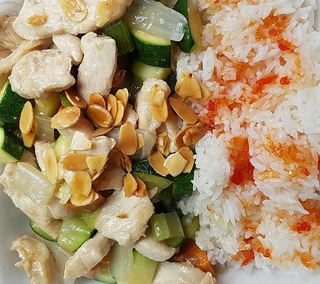 Chicken, zucchini, rice, and peanuts on a white plate.