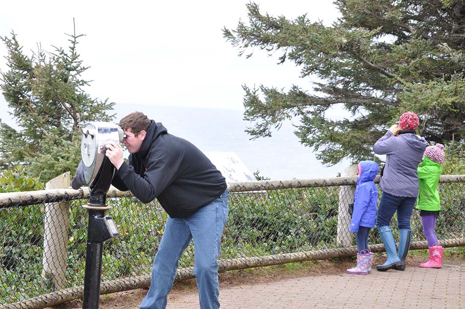 photo of woman with two children looking out to the ocean with binoculars and man using a view finder