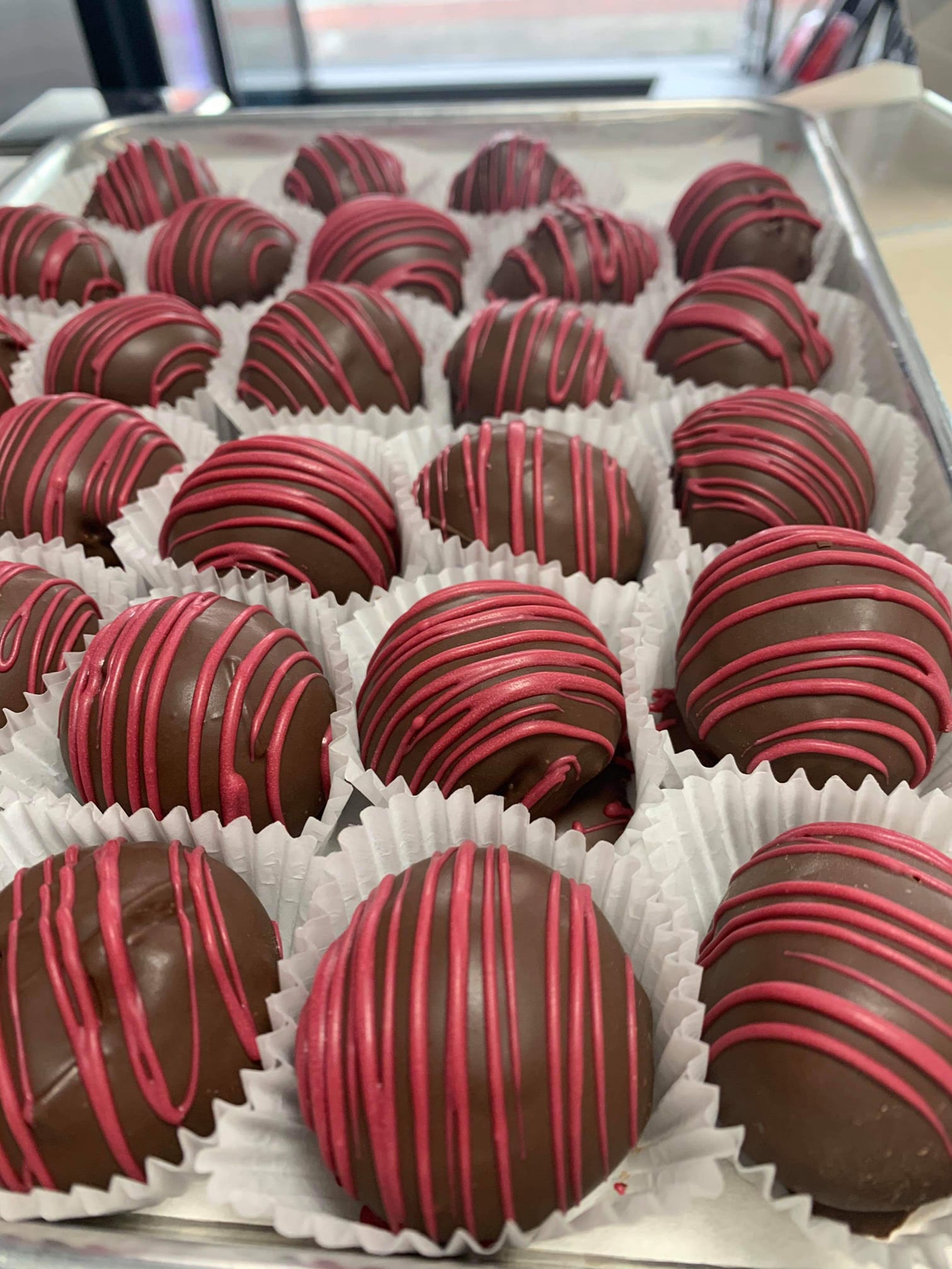 Chocolate truffles from Sweet Street Boba decorated with pink chocolate drizzle and arranged in paper cups on a tray ready for serving or gift boxes.