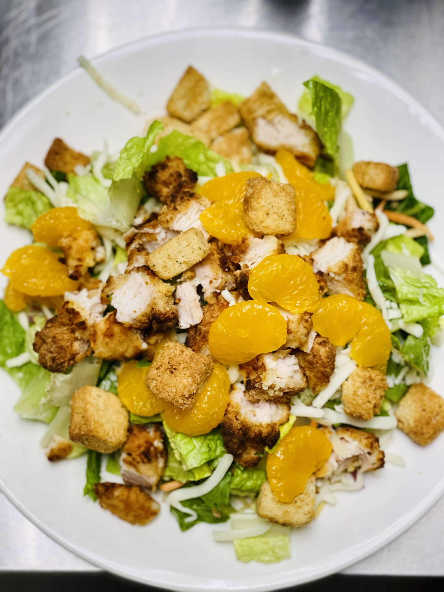 white plate with romaine greens grilled chicken croutons mandarin oranges and cheese
