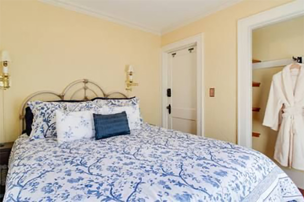 Bedroom with blue floral bedspread, bedside lamps, and robe in closet.