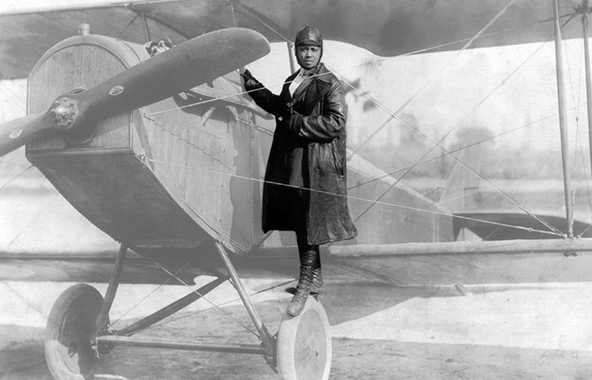 A woman stands on the wheel of an old fashioned airplane.