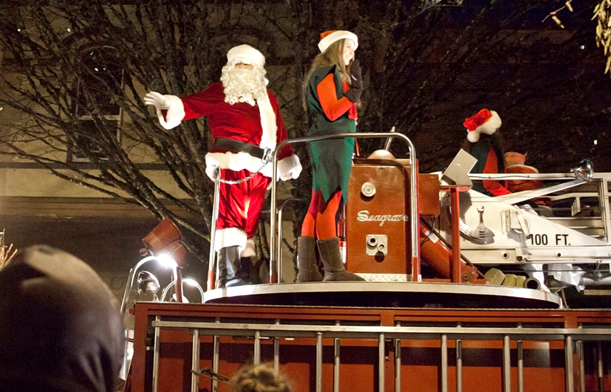 Santa and his elves stand atop an old and beautiful red fire engine.
