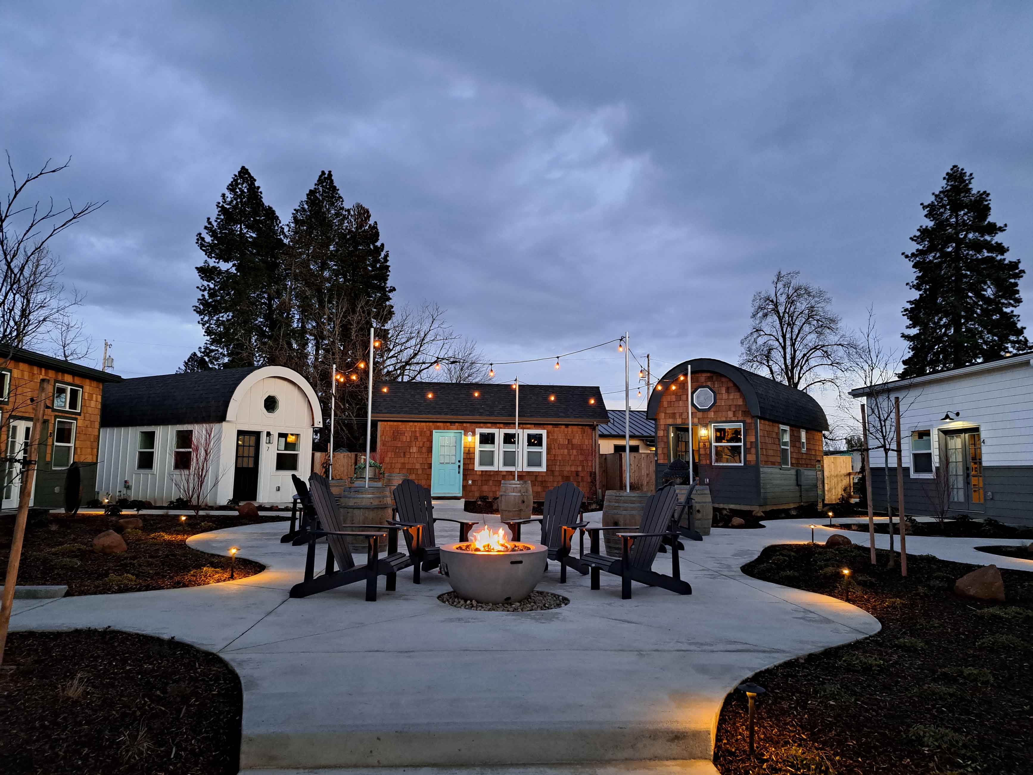 5 tiny homes are circled around a courtyard with a firepit and adirondack chairs at dusk.