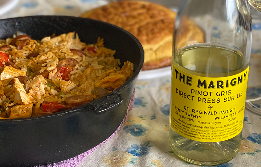 A bottle of Marigny Pinot Gris sits on a table next to a cast iron pot of jambalaya.