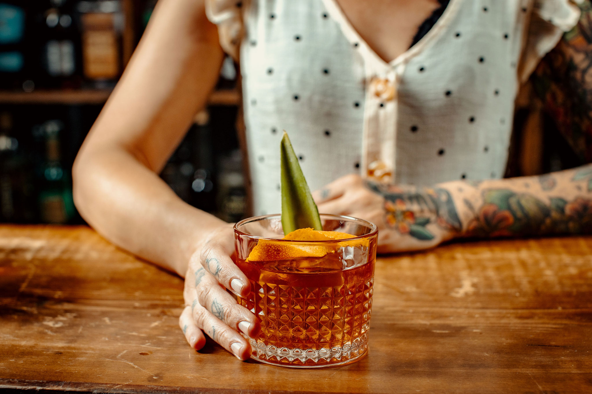 A woman holds a cocktail with orange peel garnish.