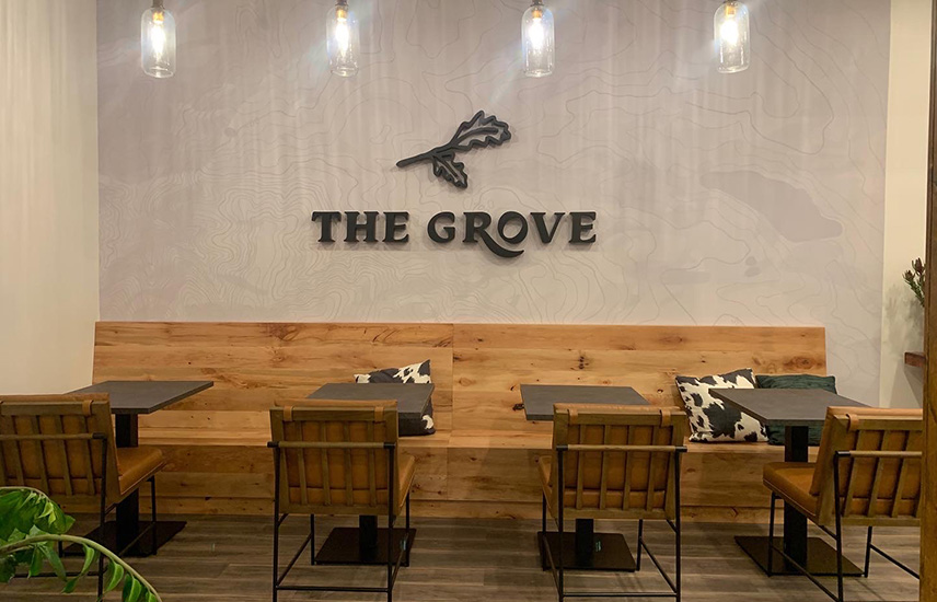 A bench stretches across a wall with the logo of The Grove. Tables and chairs sit across from the bench.