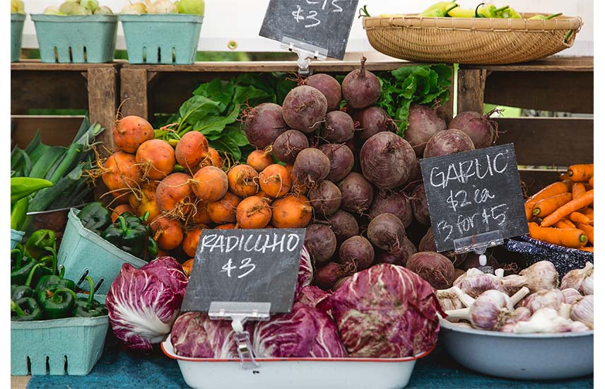 close up of farmers market produce stall with garlic, radicchio, beets, carrots and green peppers on display