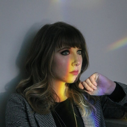 A woman looks off in the distance.  A rainbow of light shines on her face.