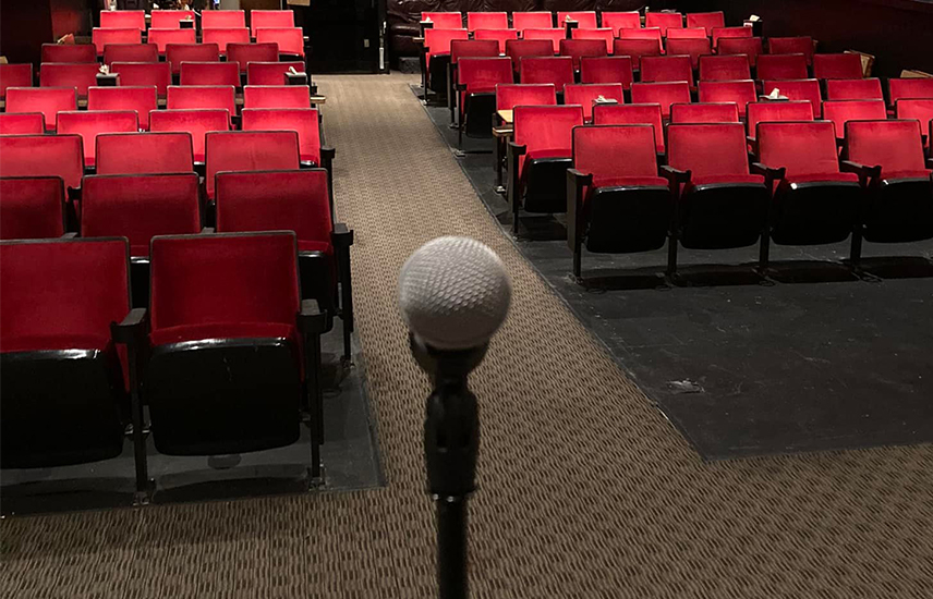 A microphone is in the foreground with rows of red theater seats in the background.