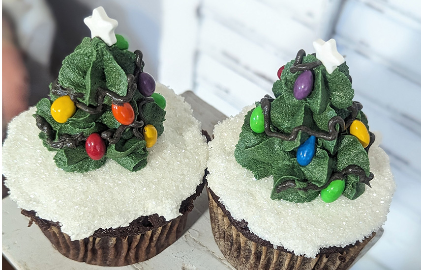 Two cupcakes with frosting trees sitting atop white snowy frosting.