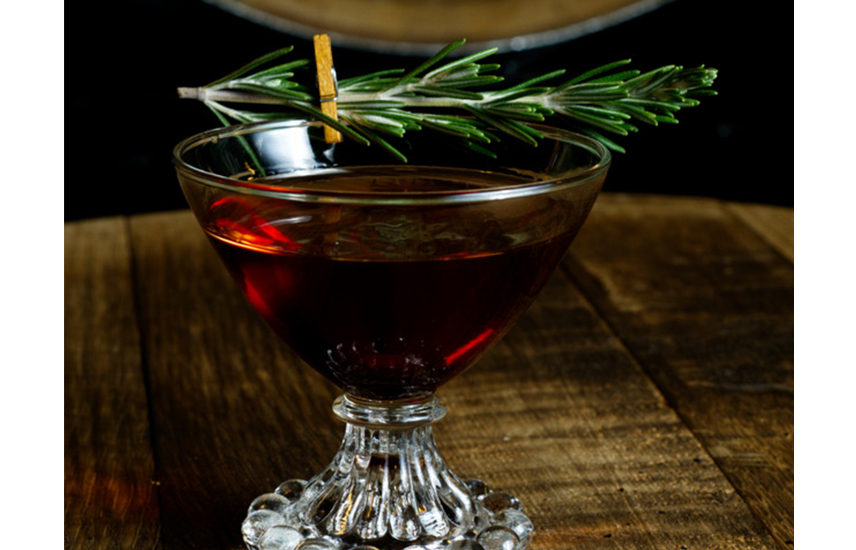 A whisky cocktail with a sprig of rosemary clipped to the rim.