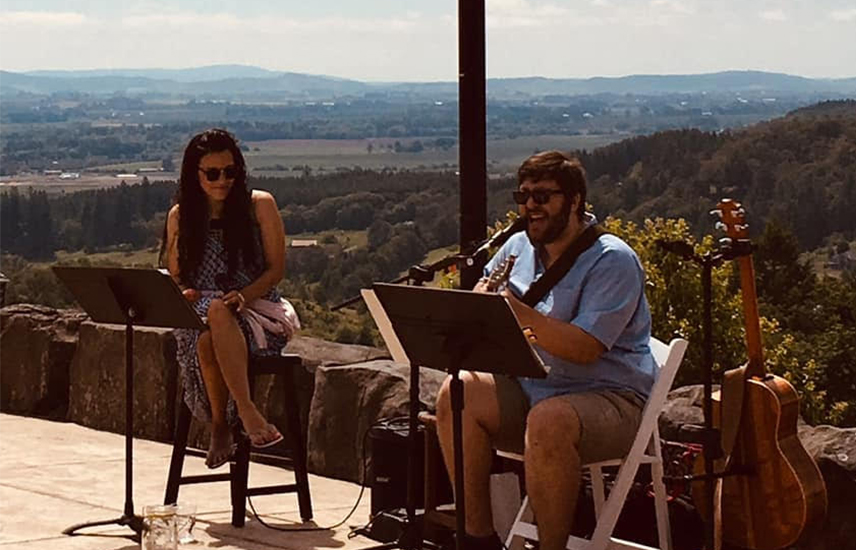 two musicians perform on outdoor patio overlooking landscape of rolling hills