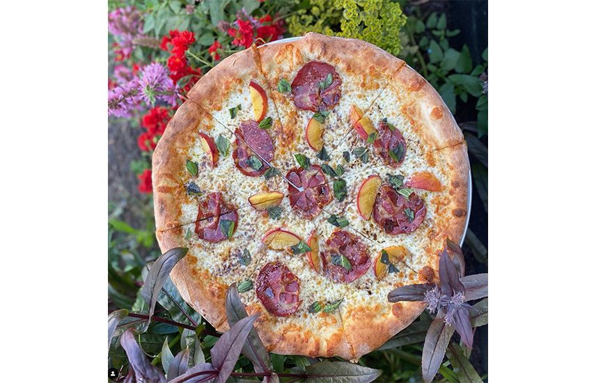 A pizza with peaches, meat, basil and cheese