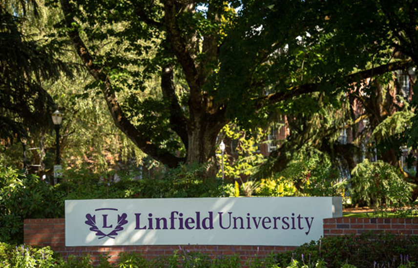 Linfield University monument nestled amongst trees and shrubs.
