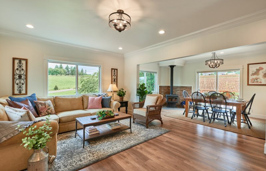 A living room with a sectional couch and a dining room in the background with a wood stove.